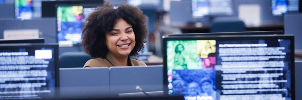A student sitting in a computer lab smiling at the camera.