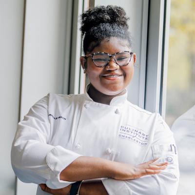 Young student wearing a culinary jacket smiling at the camera.