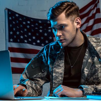 A man in military attire works on a laptop.
