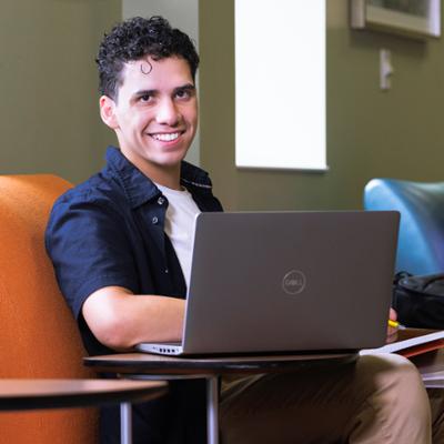 Student smiling at the camera while sitting infront of a laptop.